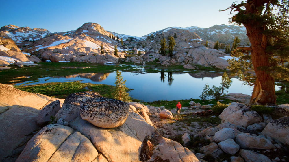 An alpine lake at sunrise. The lake is surounded by granite slabs covered in snow.