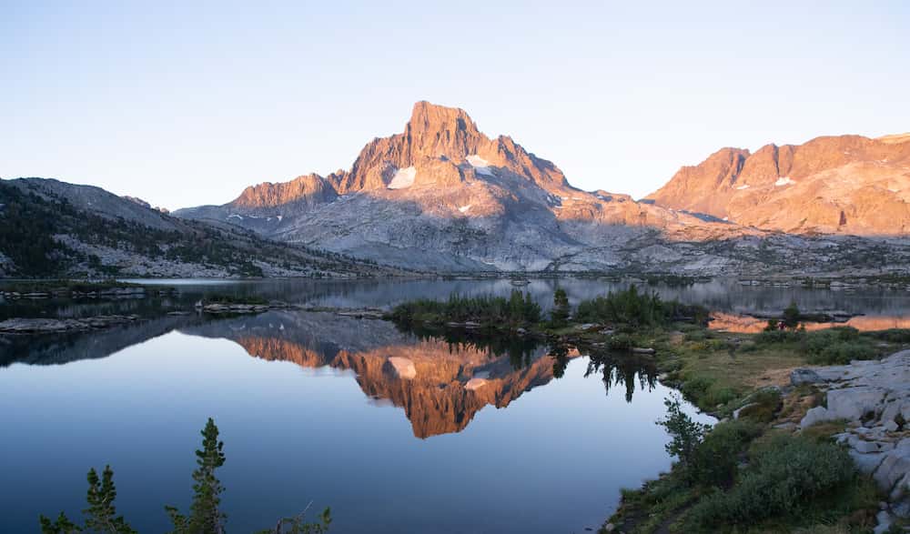Sunrise over Thousand Island Lake. Banner Peak is towering over the lake, partially lit by the sun. Its reflection is visible in the lake.